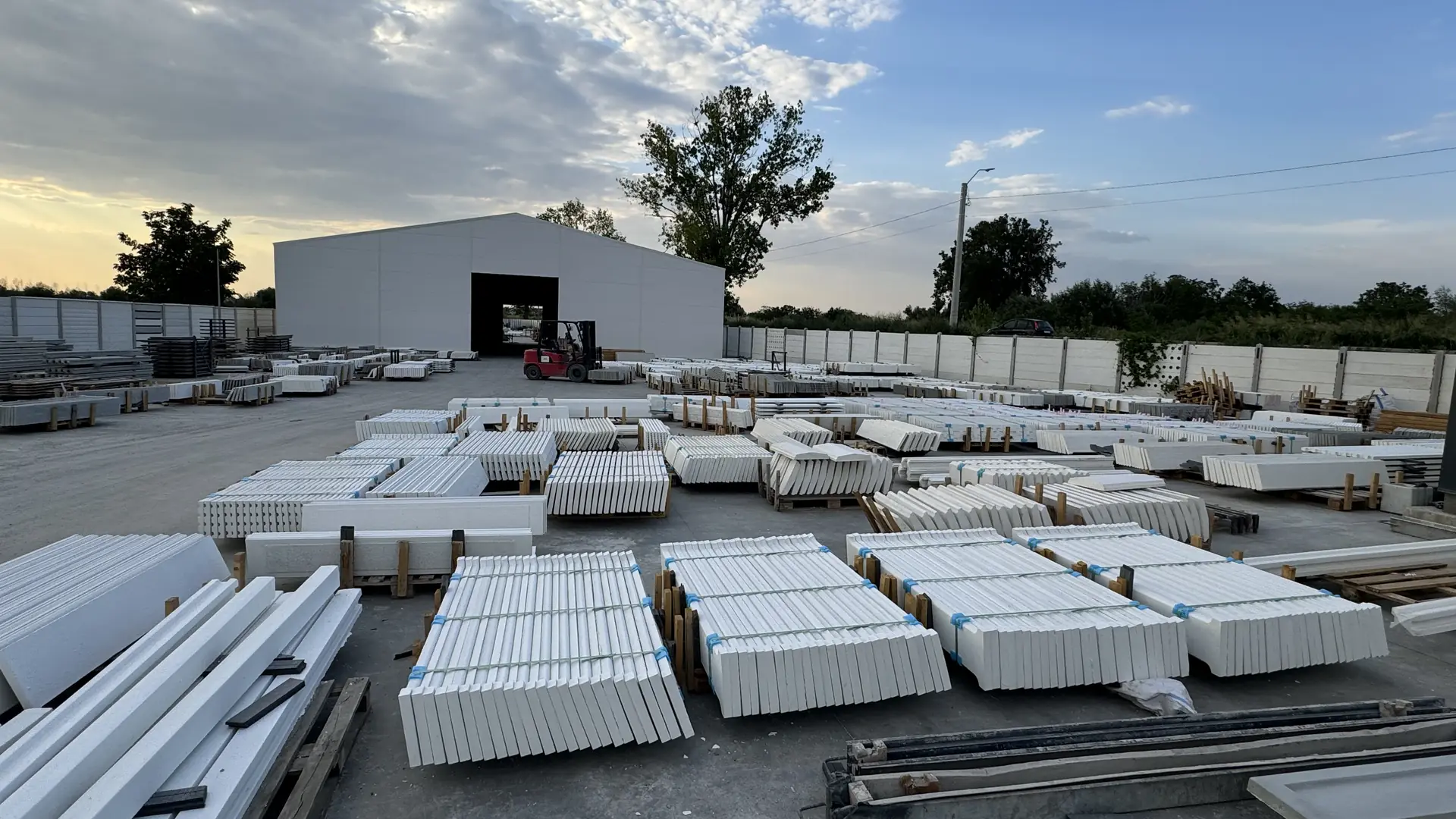 A Konkret Line măgurelei gyárának udvara alkonyatkor: kész fehér kerítéselemek raklapokon a csarnok előtt