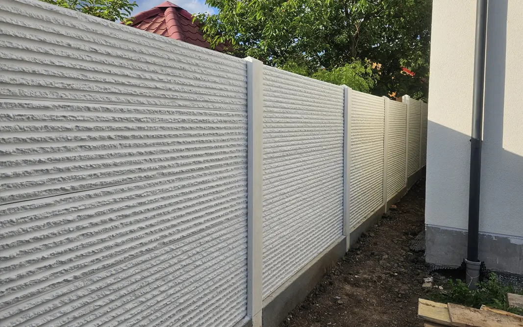 Fehér betonkerítés domborműves kerítéselemekkel egy ház mentén