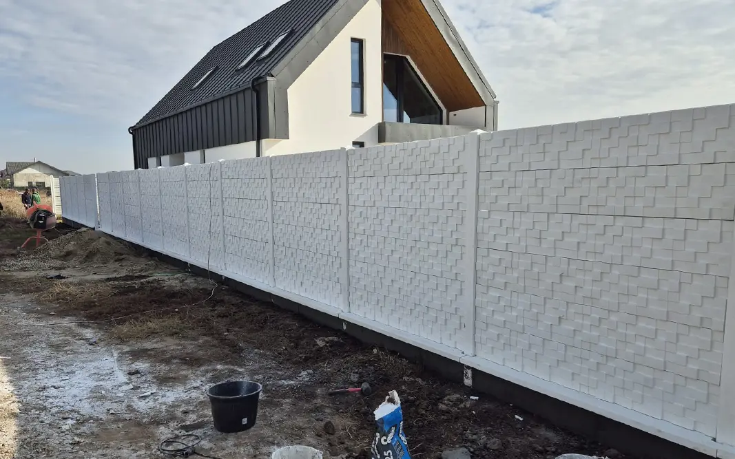Fehér betonkerítés geometrikus domborművel egy modern ház előtt